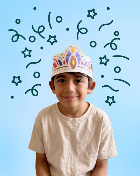 A smiling child wears a Royal Crown - Wearable & Reusable Colouring Crown featuring their own custom colouring, surrounded by floating star and confetti illustrations.
