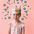 A child wearing a HeyDoodle Australia Happy Birthday reusable silicone colouring crown, decorated with a sun illustration surrounded by illustrated confetti and stars.