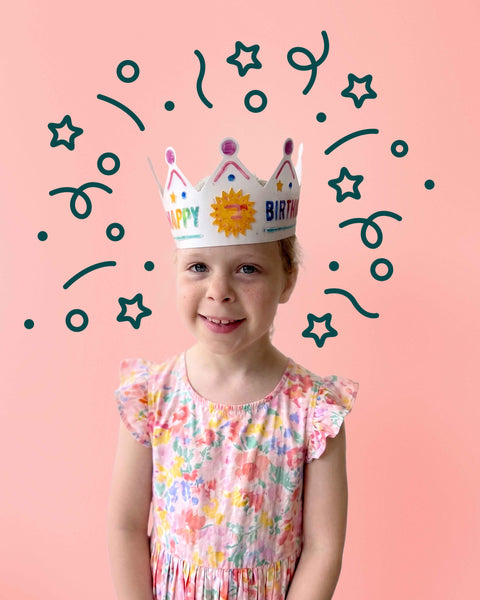 A child wearing a HeyDoodle Australia Happy Birthday reusable silicone colouring crown, decorated with a sun illustration surrounded by illustrated confetti and stars.