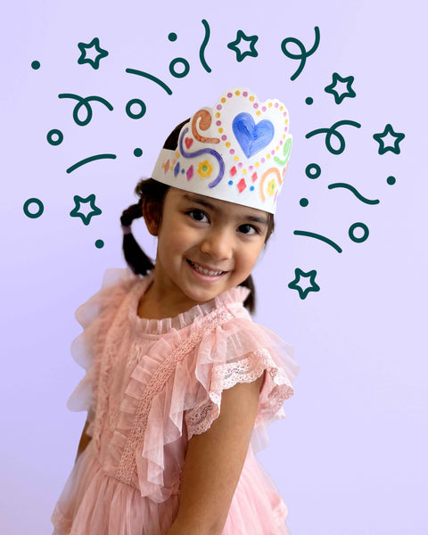 A young girl smiles while wearing a HeyDoodle Australia Tiara Hearts, an adjustable silicone crown featuring hand-drawn hearts and swirls designed to be coloured and reused.