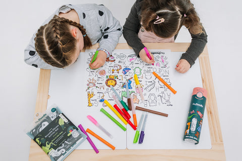 two girls drawing on Into the wild classic heydoodle mat with crayons, on a table