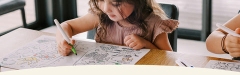 Child colouring at a table with heydoodle colouring mat and markers