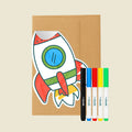 Rocket-shaped Reusable Gifting Card™, an envelope and five markers on a beige background