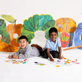 Two young boys sit on the floor, smiling as they draw with colourful markers on a HeyDoodle Australia The Very Hungry Caterpillar™ Classic Colouring & Doodle Mat. Behind them, lively, vibrant fruit and the beloved caterpillar character from The Very Hungry Caterpillar brighten the scene. Their creativity comes alive on this reusable silicone mat, featuring playful patterns and vivid colours designed to inspire imagination and provide a fun, screen-free colouring activity for children.