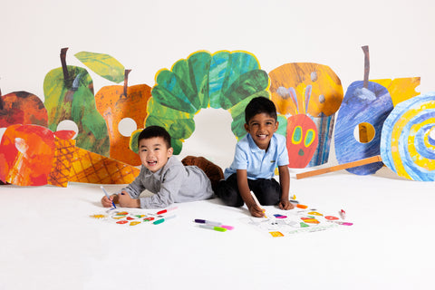Two young boys sit on the floor, smiling as they draw with colourful markers on a HeyDoodle Australia The Very Hungry Caterpillar™ Classic Colouring & Doodle Mat. Behind them, lively, vibrant fruit and the beloved caterpillar character from The Very Hungry Caterpillar brighten the scene. Their creativity comes alive on this reusable silicone mat, featuring playful patterns and vivid colours designed to inspire imagination and provide a fun, screen-free colouring activity for children.