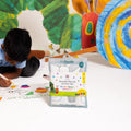A child engages with vibrant The Very Hungry Caterpillar-themed silicone mats, joyfully colouring and enjoying a screen-free creative activity. In the foreground, the HeyDoodle Australia The Very Hungry Caterpillar™ Classic Colouring & Doodle Mat package stands upright, highlighting its colourful and playful reusable silicone mat design perfect for imaginative play.