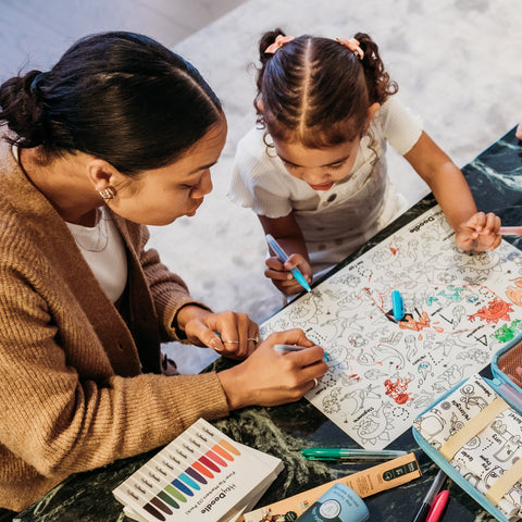 An adult and a young girl color together on a reusable silicone DinoRoar mat, markers scattered—perfect for colourful, creative fun.
