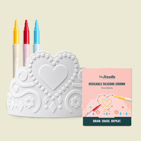 A white silicone Tiara Hearts wearable, reusable colouring crown embossed with heart and flower patterns, accompanied by three markers and its square product box.