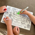 Two kids colour a reusable HeyDoodle Jingle Bells silicone mat with festive trees, gingerbread, gifts, stockings, and numbers.