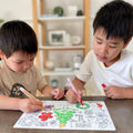 Two boys color the reusable HeyDoodle silicone mat, featuring a festive tree and holiday designs. 