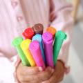 A child in a light pink shirt holds vibrant crayon pens with multicolored caps, perfect for reusable colouring.