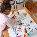 A young child colours animal counting mats at a table with crayon pens, surrounded by markers and animal figurines.