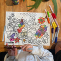 A child colours a reusable HeyDoodle silicone mat featuring native floral patterns, using vibrant markers spread on a wooden table.