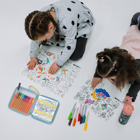 Two children colouring on HeyDoodle Mats with markers and travel case on a white floor.