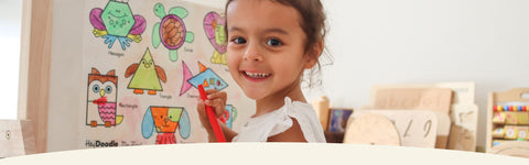 Child holding a red crayon in front of a my first mat with animal illustrations.