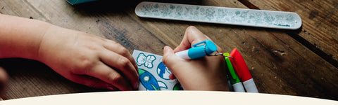 Children's hands colouring party favours stickers with markers on a wooden table