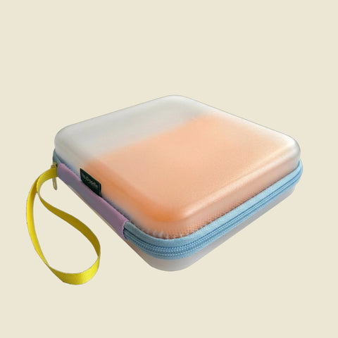 A pastel silicone HeyDoodle Australia Travel Case POS Listing with a translucent lid, blue zipper, and yellow wrist strap on beige.